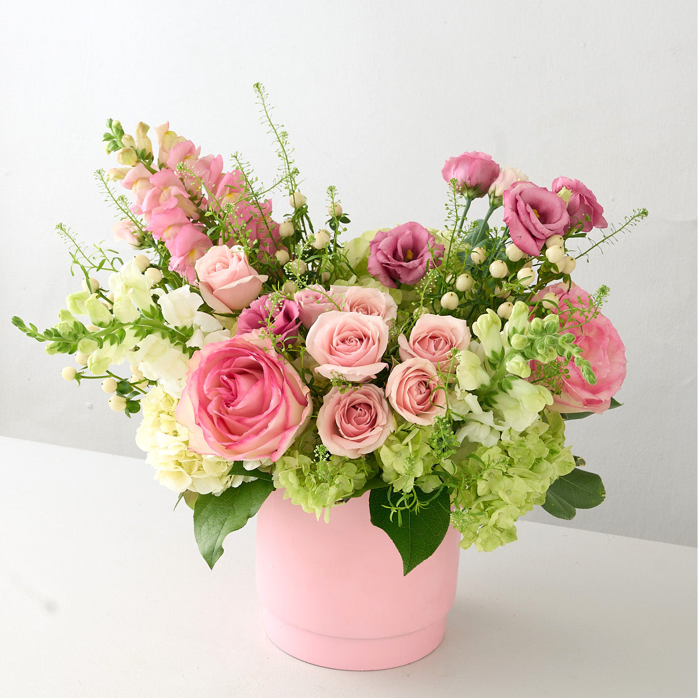 up close photo of a pink ceramic vase with pink snap dragons, lisianthus, roses and white flowers.