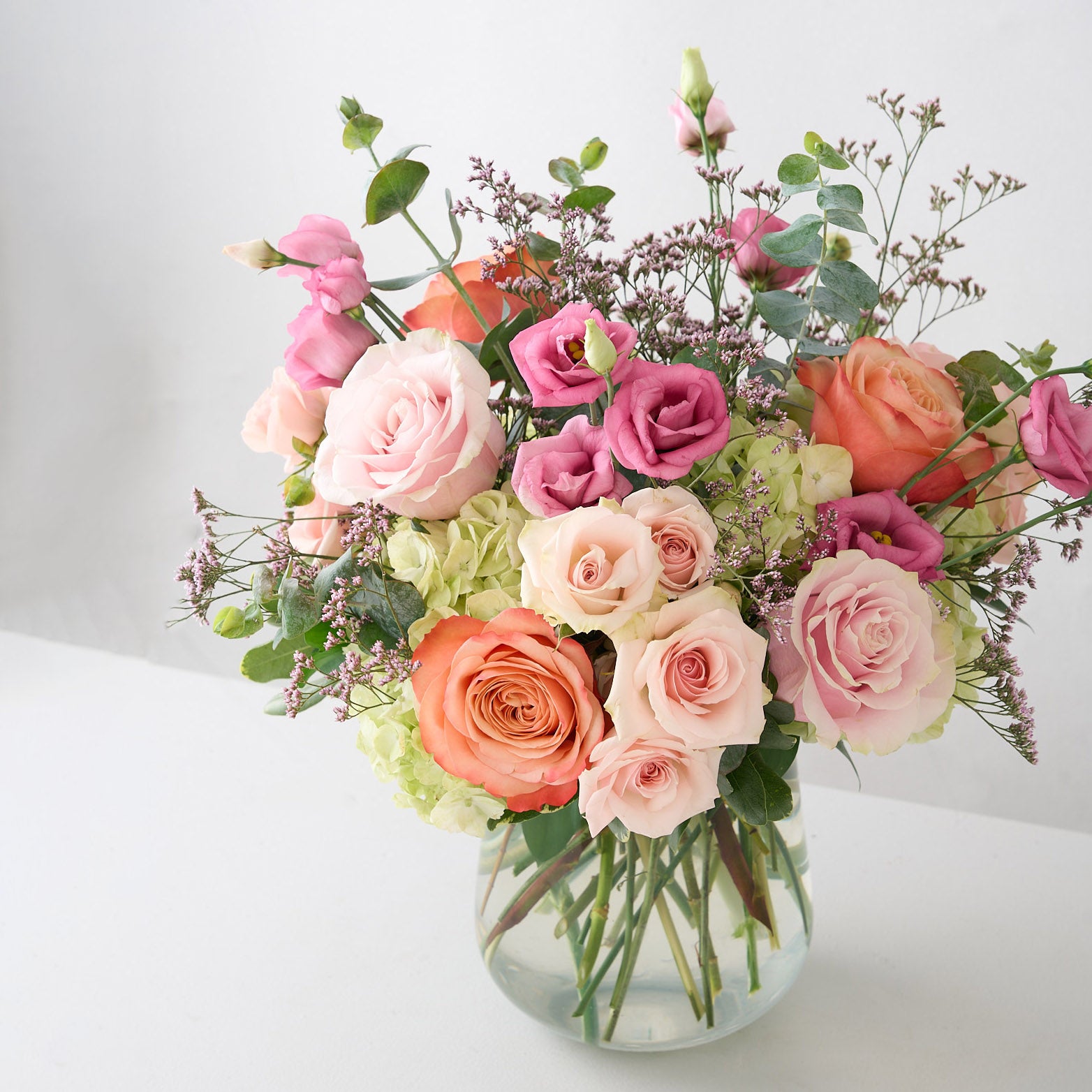 mother's day arrangement with pink and coral roses, rose lisianthus; and white hydrangea on a white table