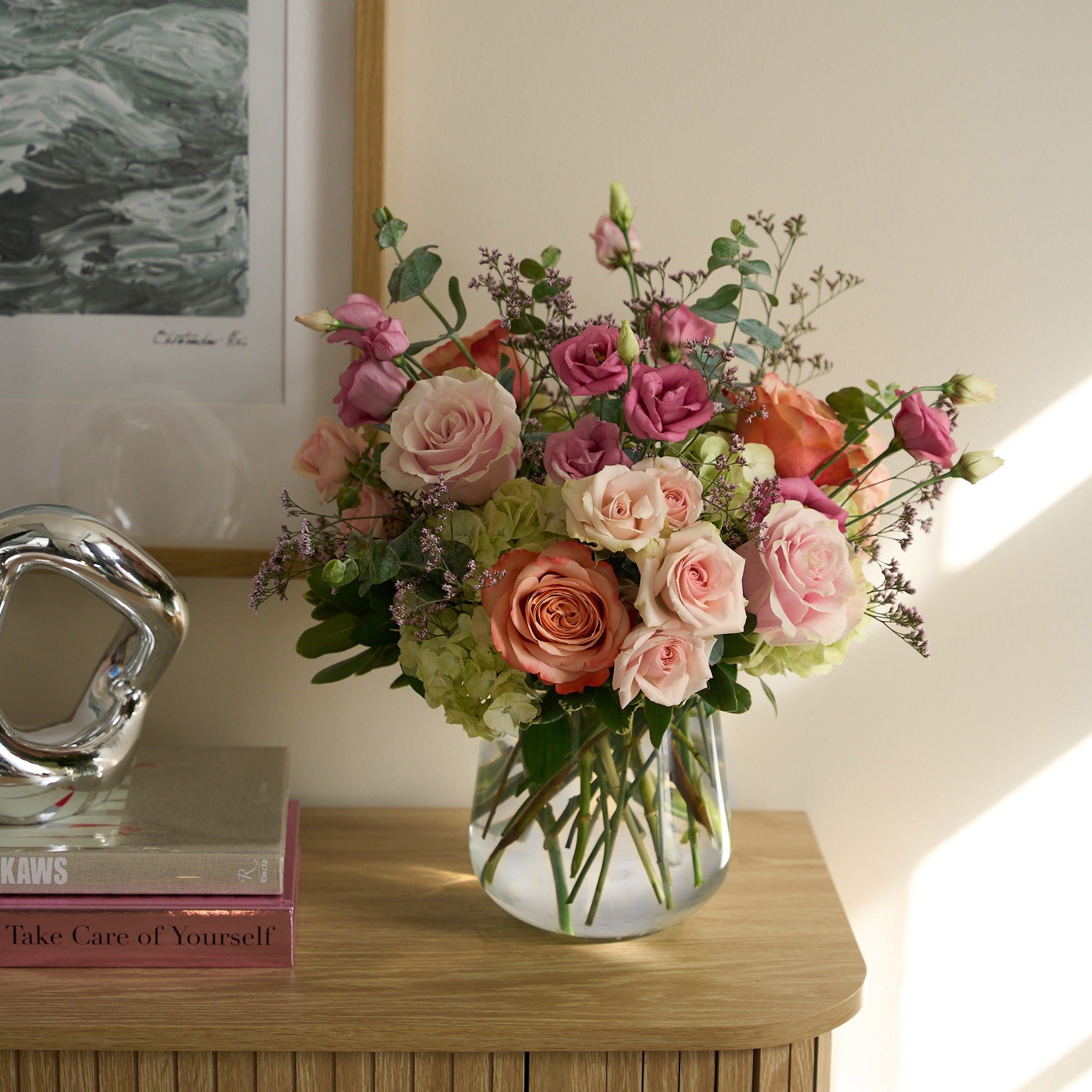 mother's day arrangement with pink and coral roses, rose lisianthus; and white hydrangea on light beige credenza. 