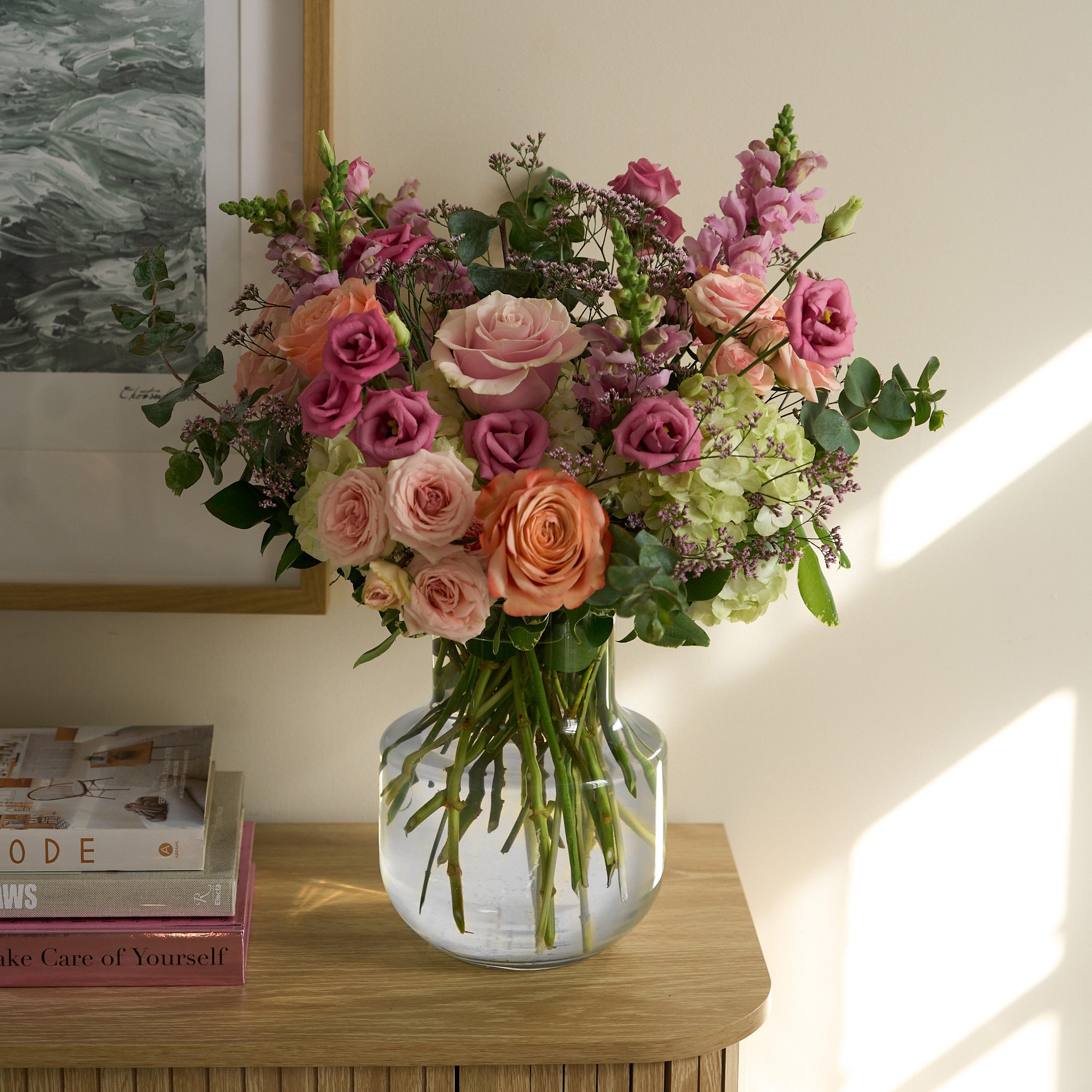 Bouquet of pink, orange, and green flowers in a clear vase on a beige credenza.