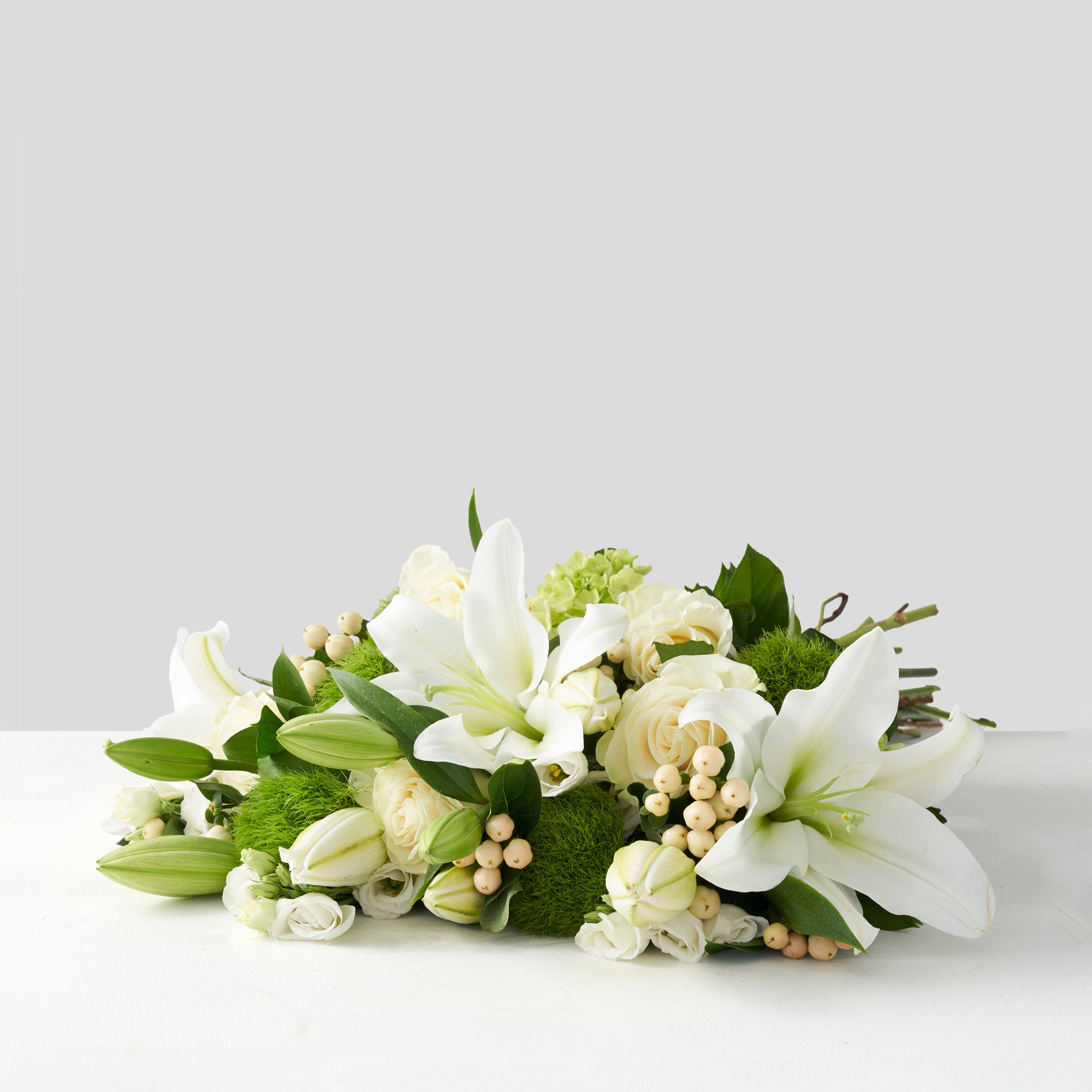 Bouquet of white Mondial roses, white lilies, cream berries and green hydrangea on a white background.