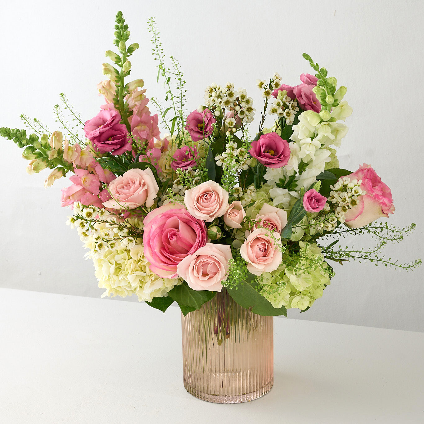 tall pink gold ribbed vase with white flowers, and pink roses and lisianthus