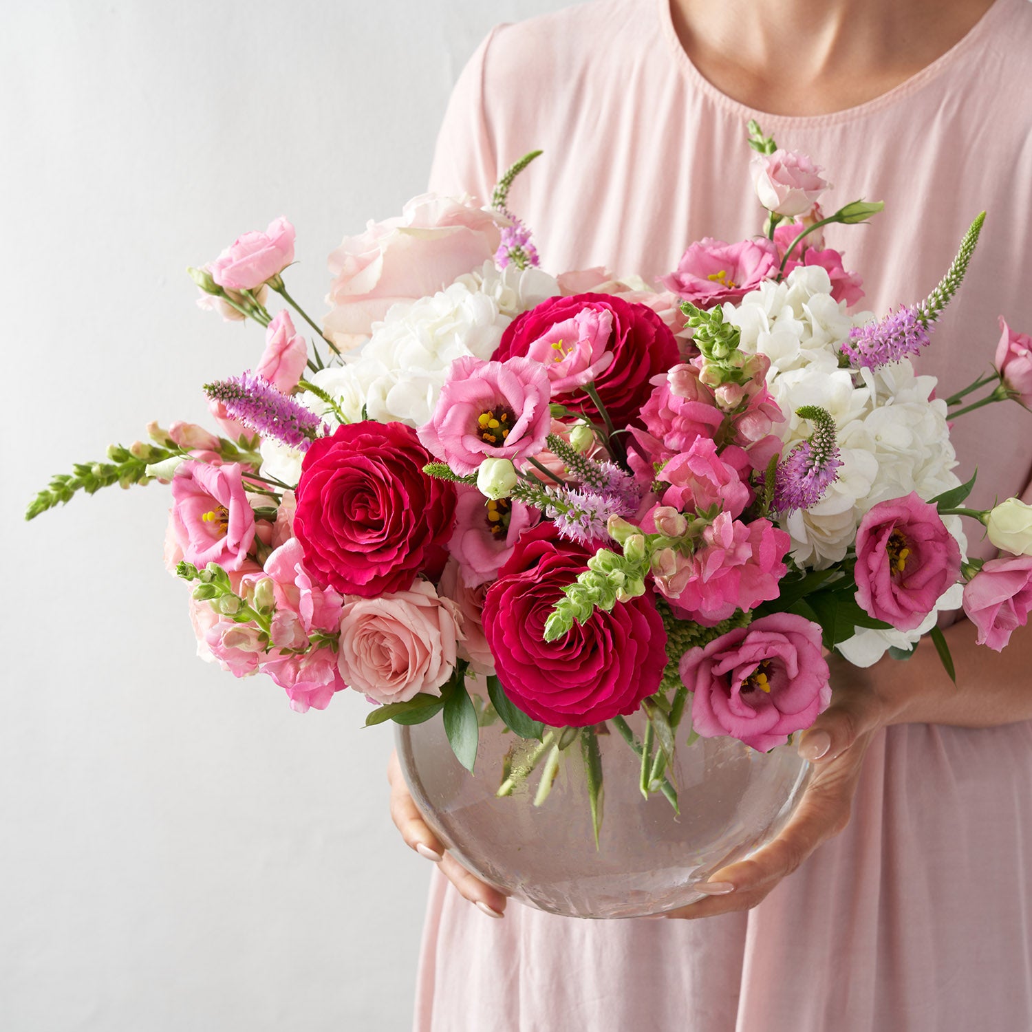 woman in pink dress holding rosebowl filled with pink flowers, including roses, lisianthus and snapdragons.
