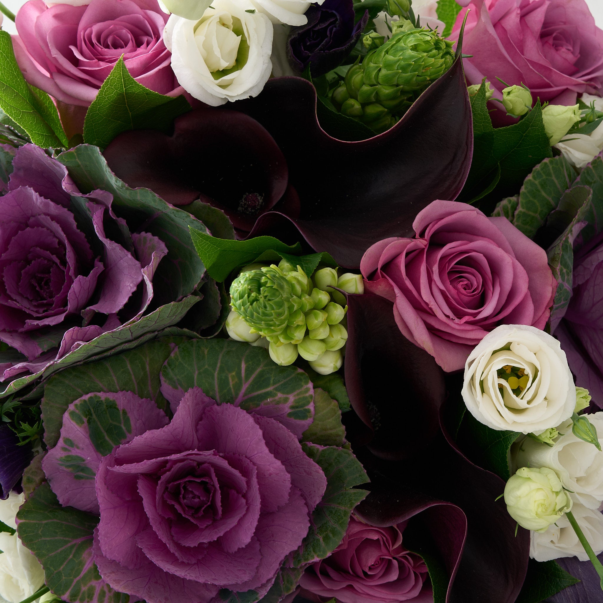 close up picture of a bouquet of purple, maroon, and white flowers with greens.