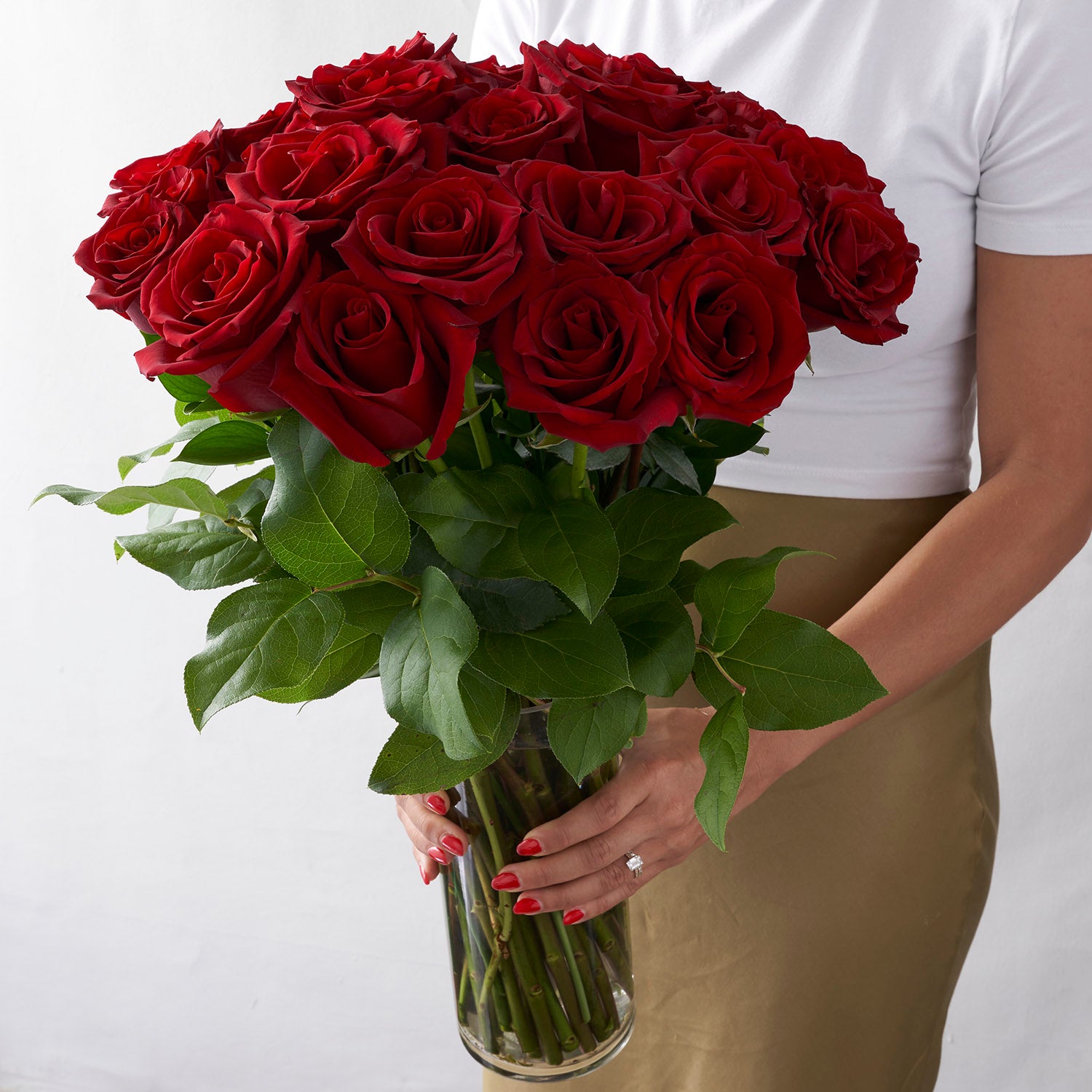 Woman holding glass vase full of red roses with greenery.