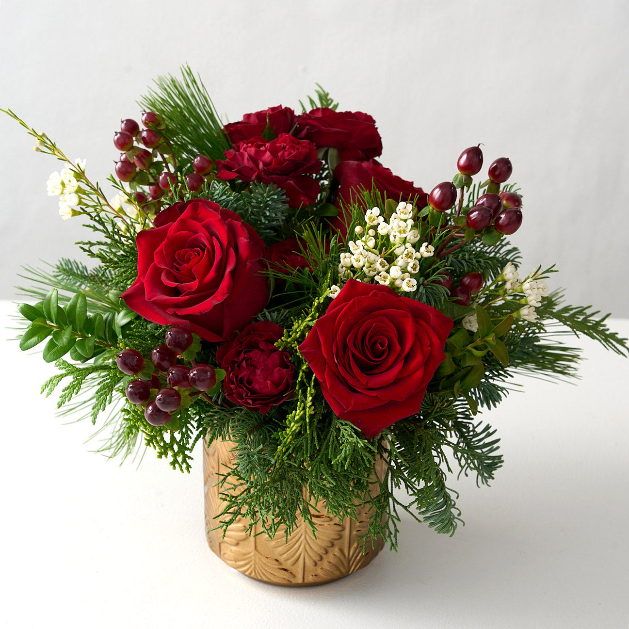 floral arrangement with red roses, hypericum, carnations and fresh boxwood, cedar branches with wax flowers in a gold pot