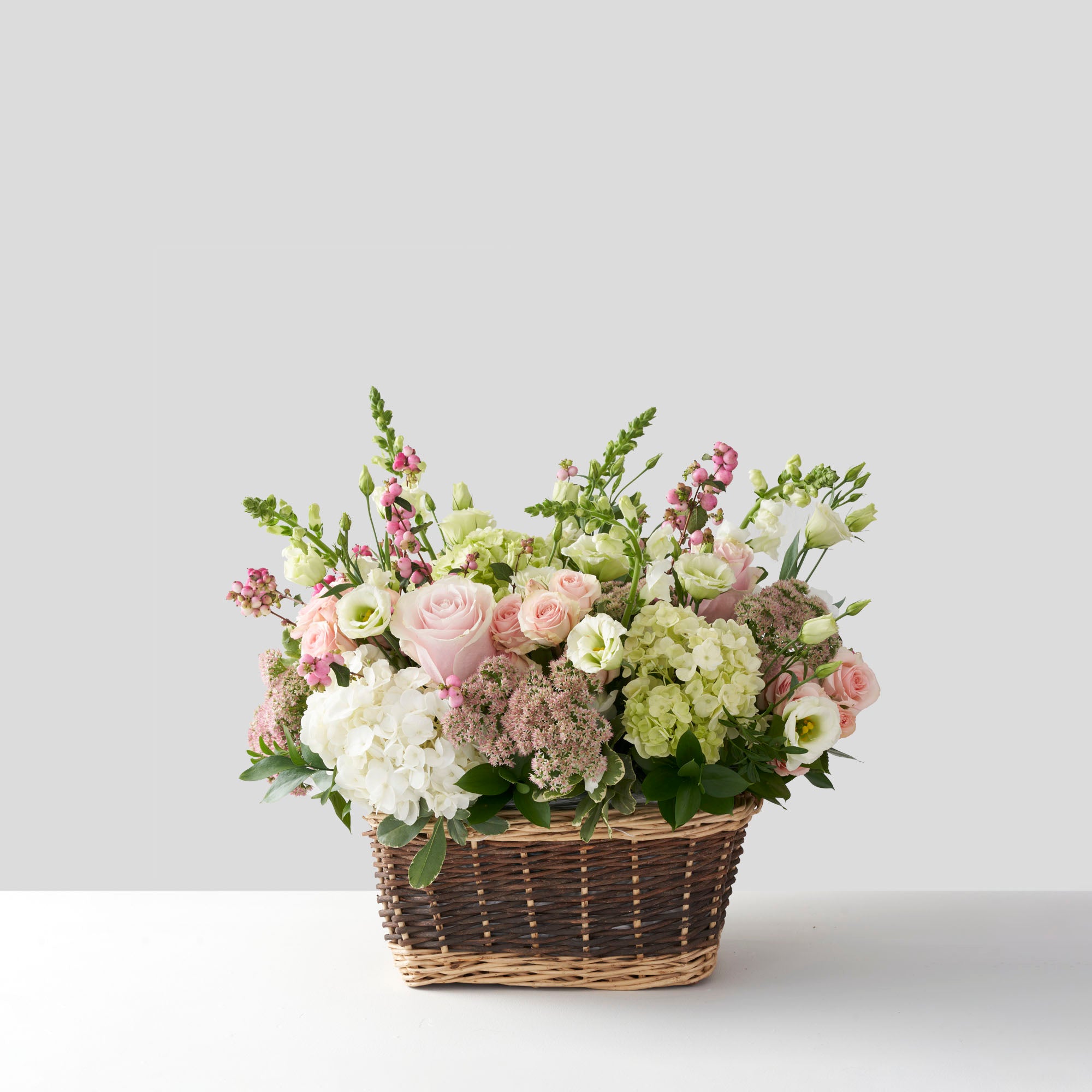 Flower arrangement of soft pink, white, and pale green, in natural basket.