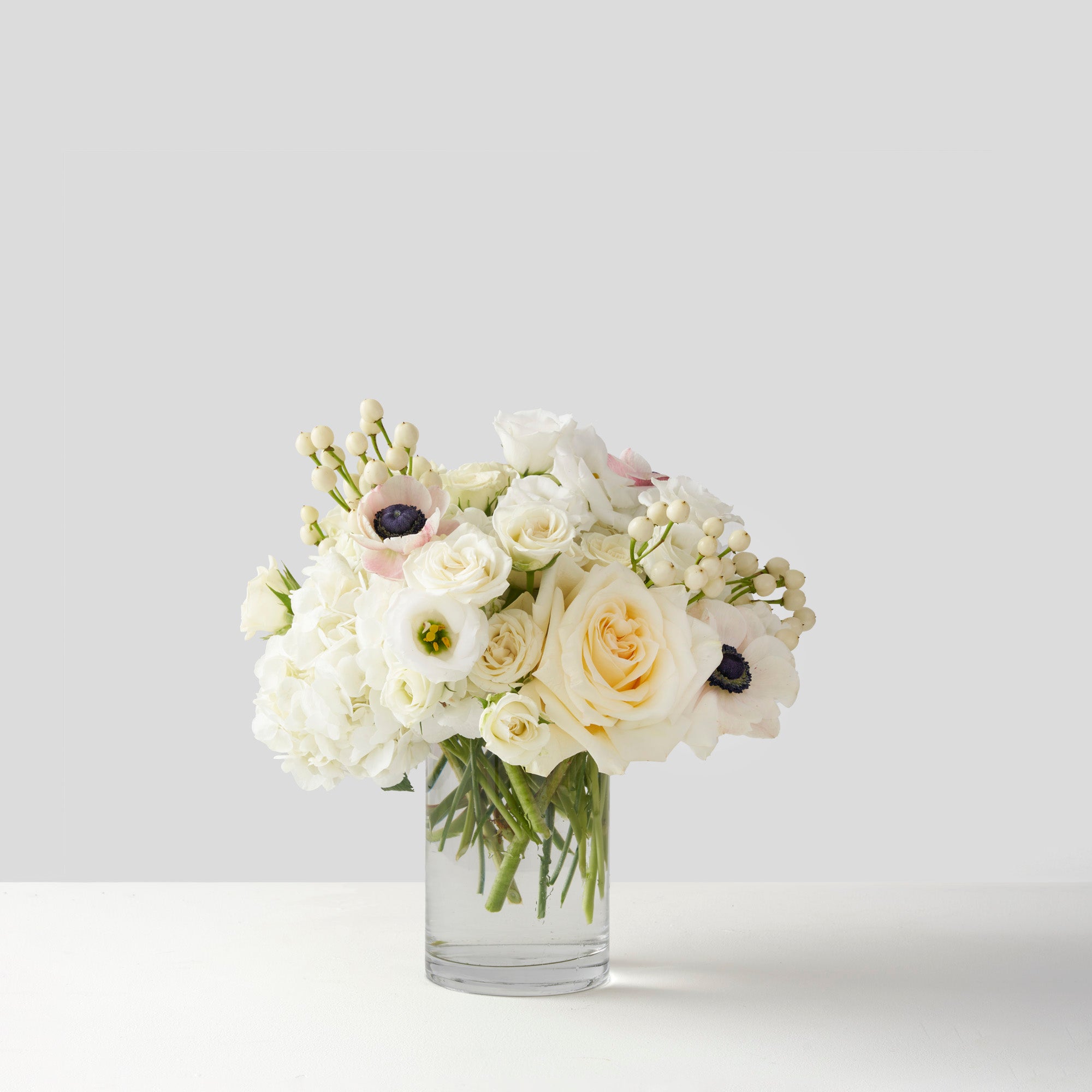Clear glass vase full of cream and white flowers on white background.