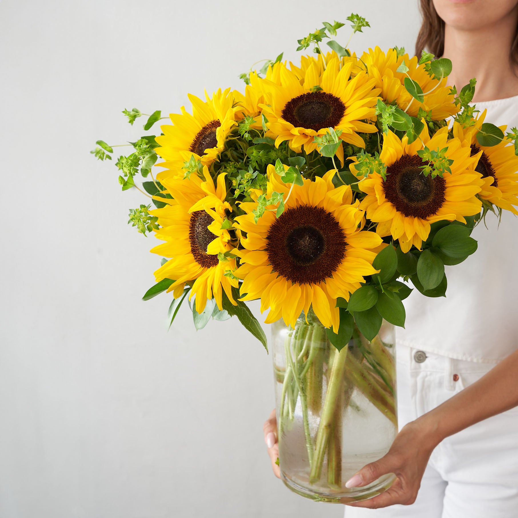 Girl in white holding sunflowers in a clear glass vase
