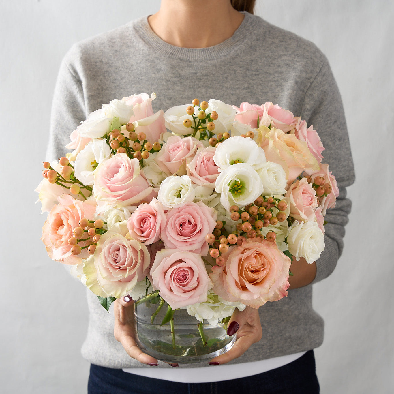 woman holding a pink, white flower arrangement in a glass vase