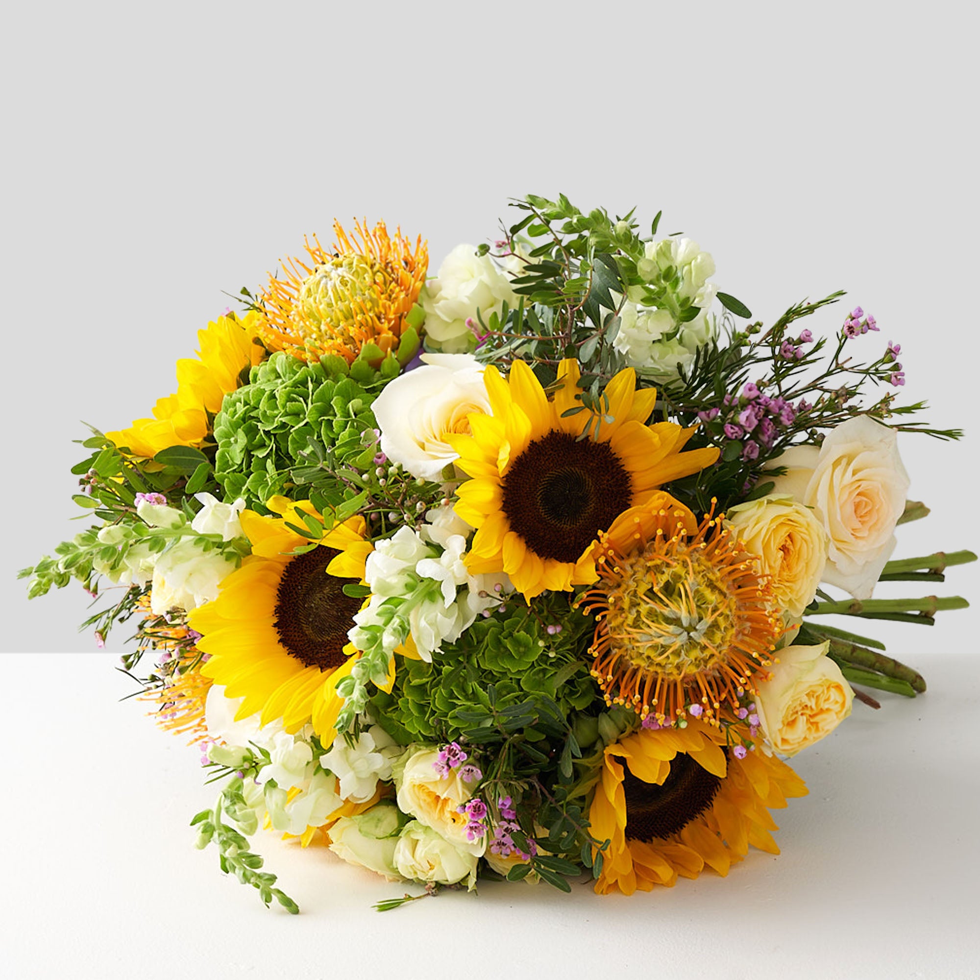 bouquet of sunflowers, proteas, white roses, spray roses, green hydrangeas, and other greenery