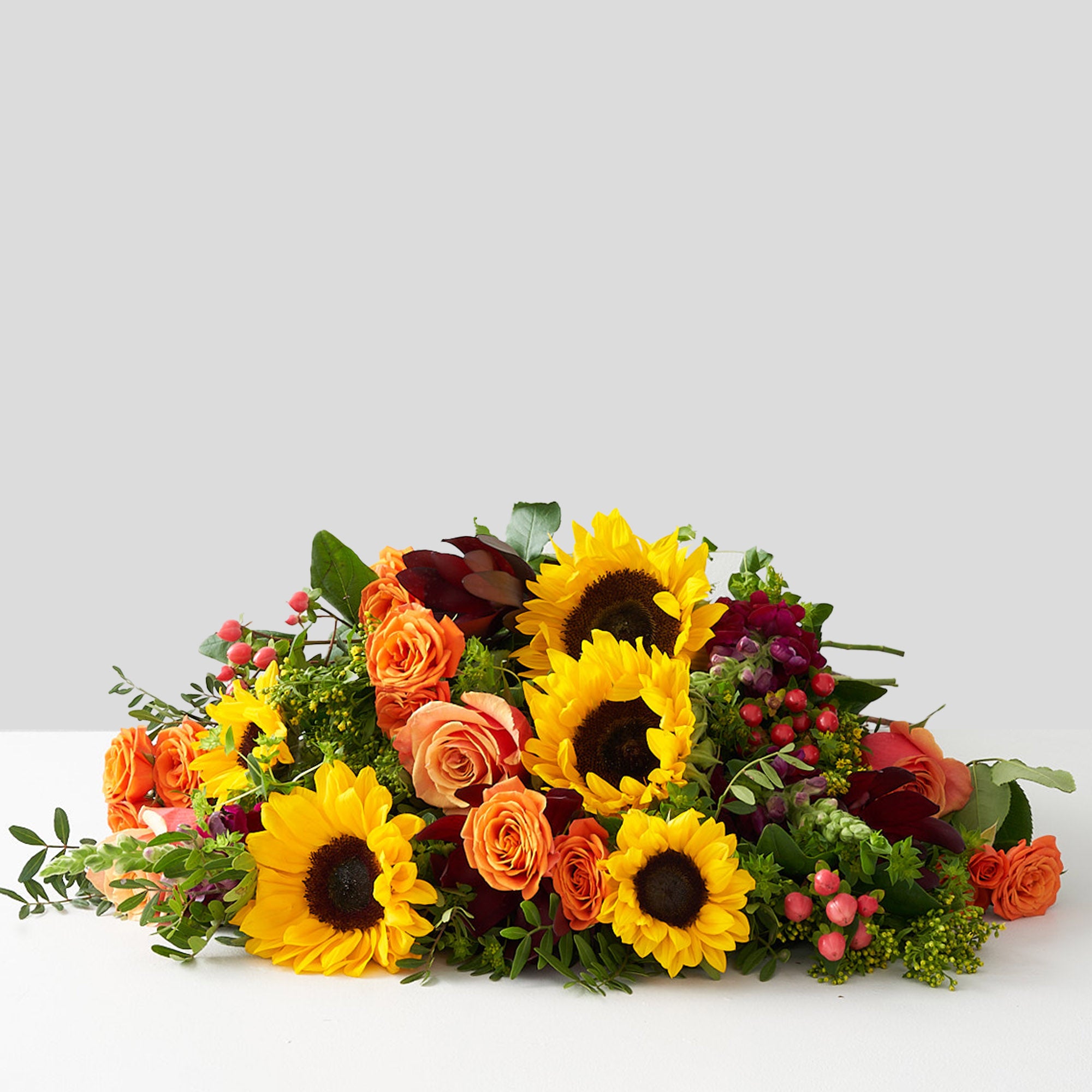 Vibrant bouquet composed of sunflowers, free spirit roses, kahala roses, red and pink hypericum berries, and other greenery