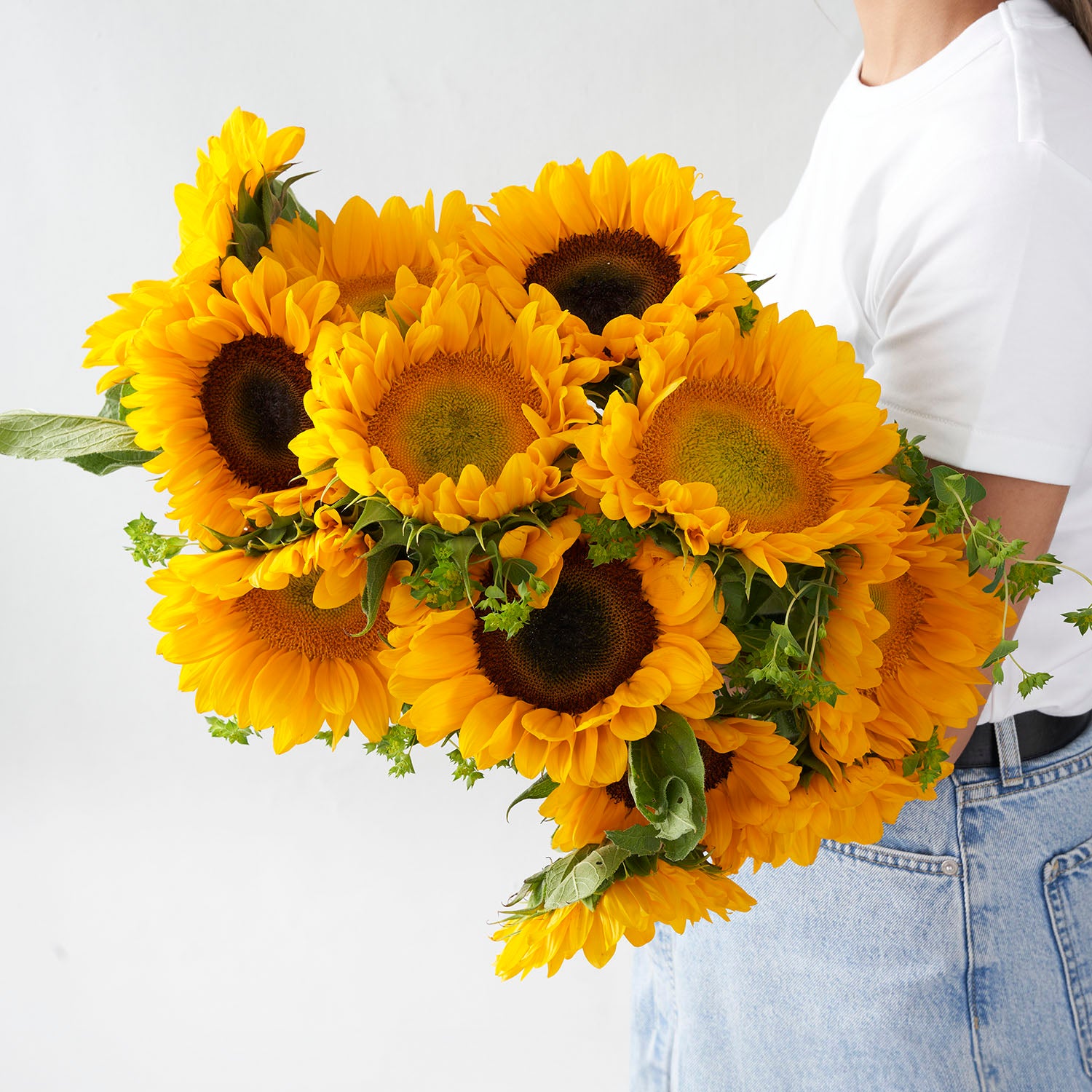 Woman in white shirt and jeans holding large bouquet of sunflowers.