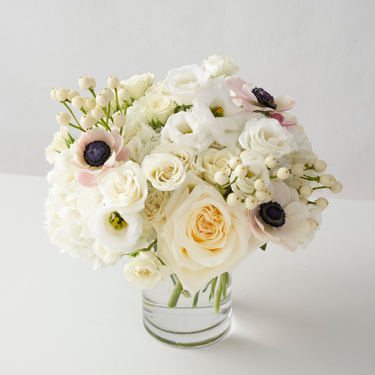 Clear glass vase of white and cream flowers, tightly arranged, centered on white background. 