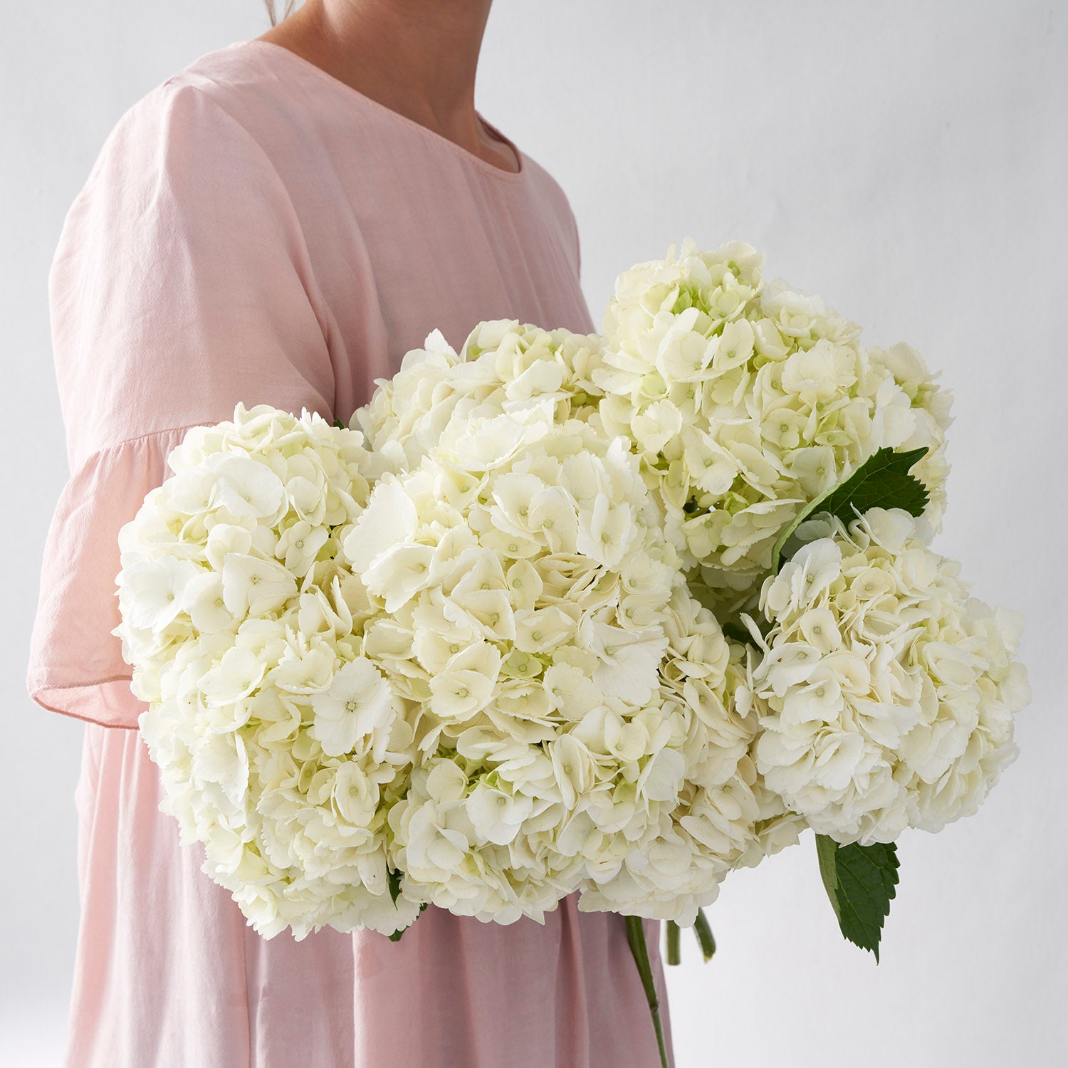 Woman in pink dress holding large bouquet of white hydrangea flowers.