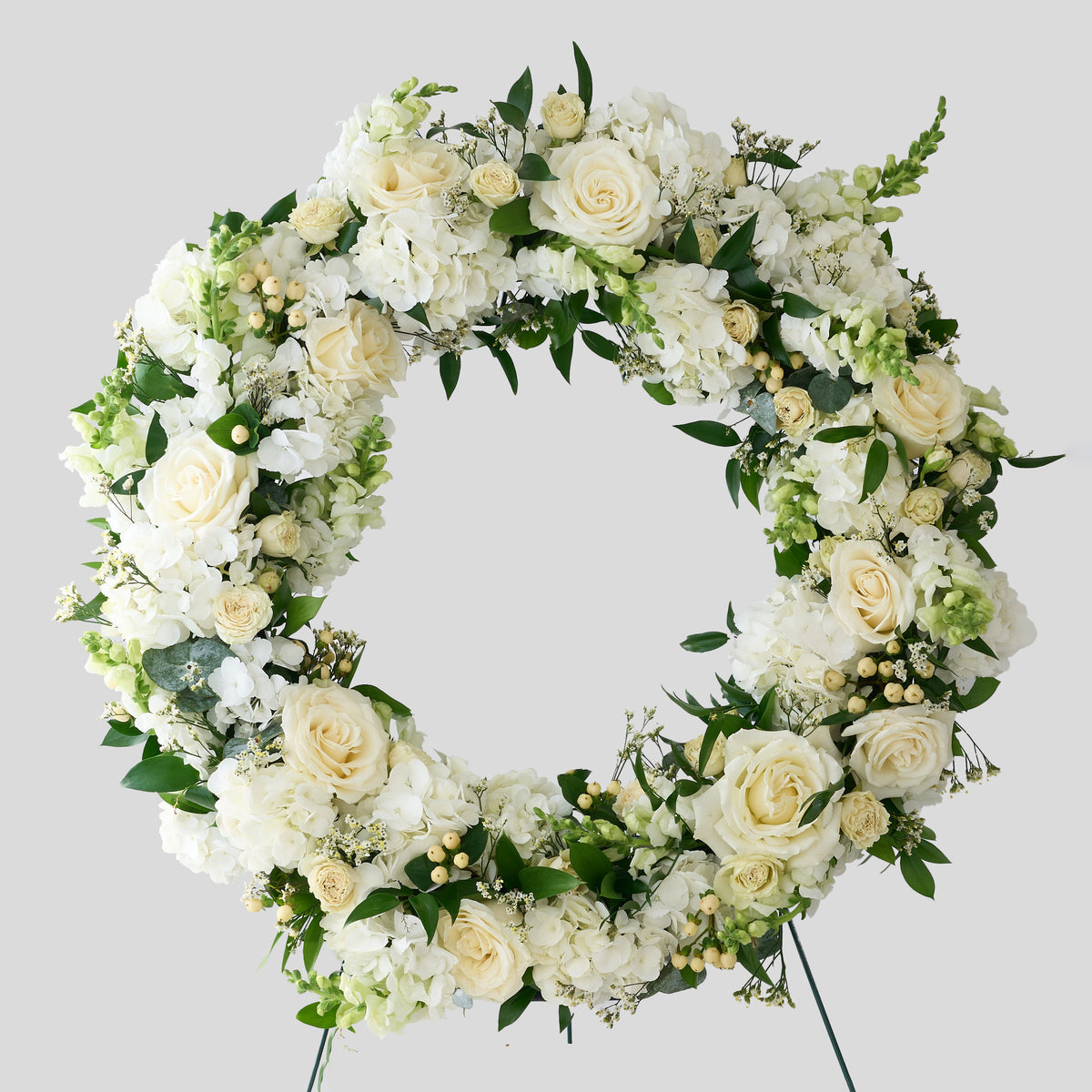 Floral funeral wreath with white hydrangea, snapdragons, hypericum berries roses and green flowers on a light gray background