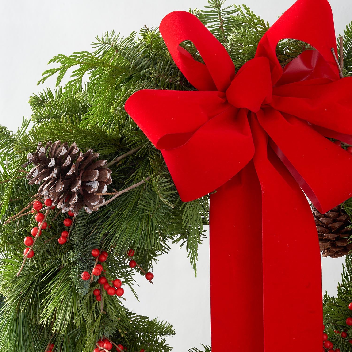 Closeup of Christmas wreath with pine cones, red ilex berries and red bow.