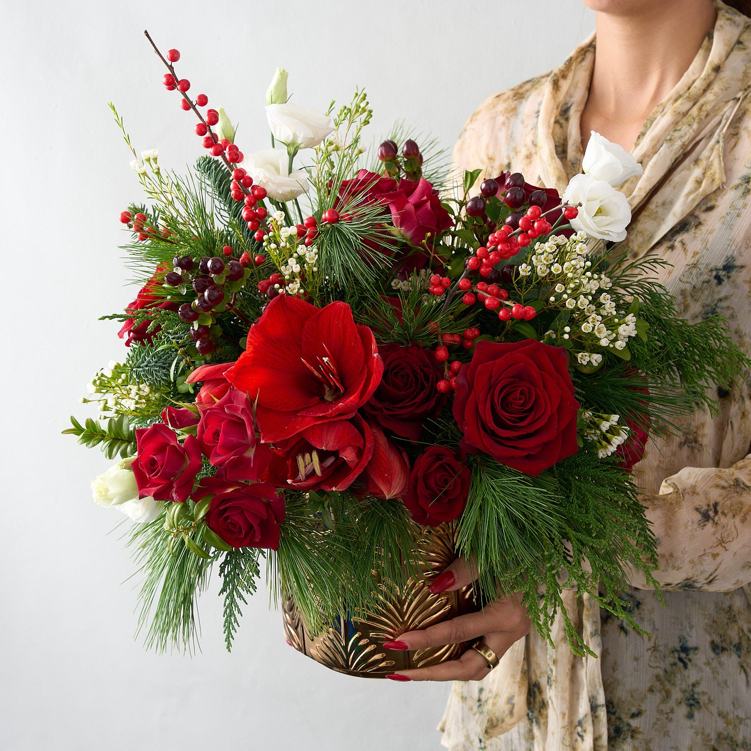 woman holding a arrangement with Christmas arrangement with red flower and white flowers with cedar, white pine and ilex berries in a gold vase