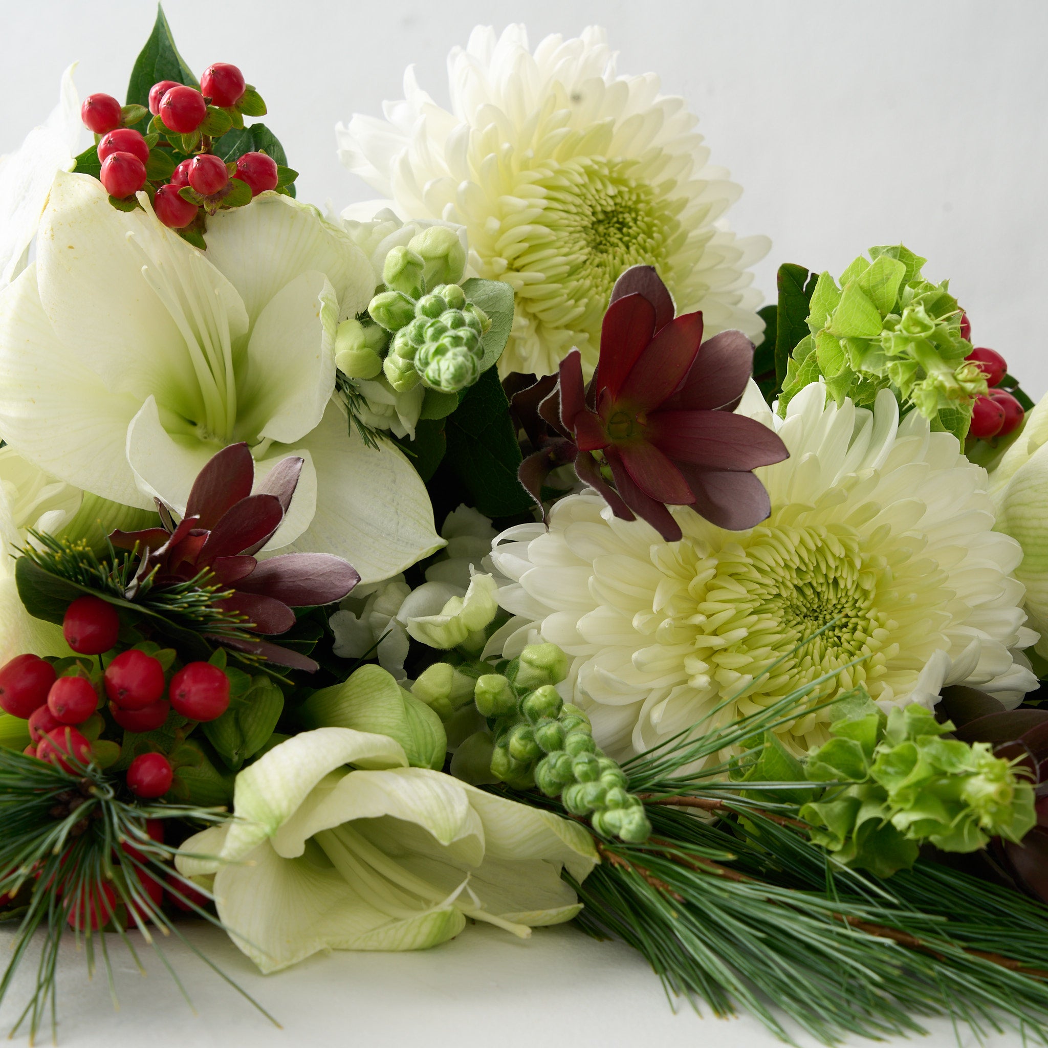 close up picture holiday bouquet with red hypericum, white mums, snap dragons and lilies with white pine branches.