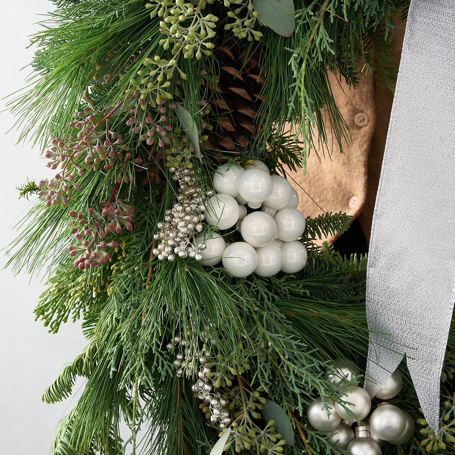 close up picture of tinsel wreath with white and silver berries and fresh cedar seeds