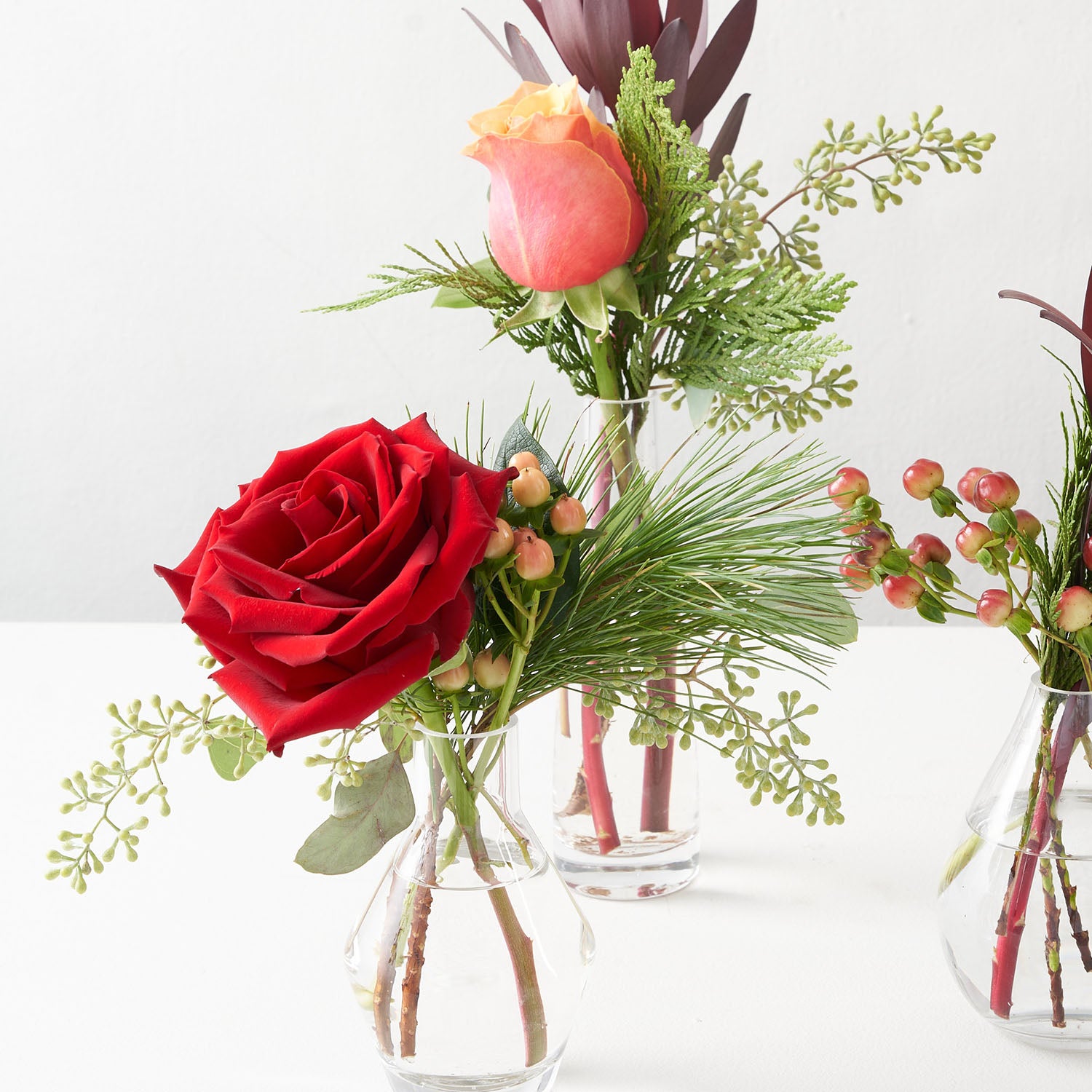 Closeup of small vases with pine, berry eucalyptus, hypericum berries, and red roses