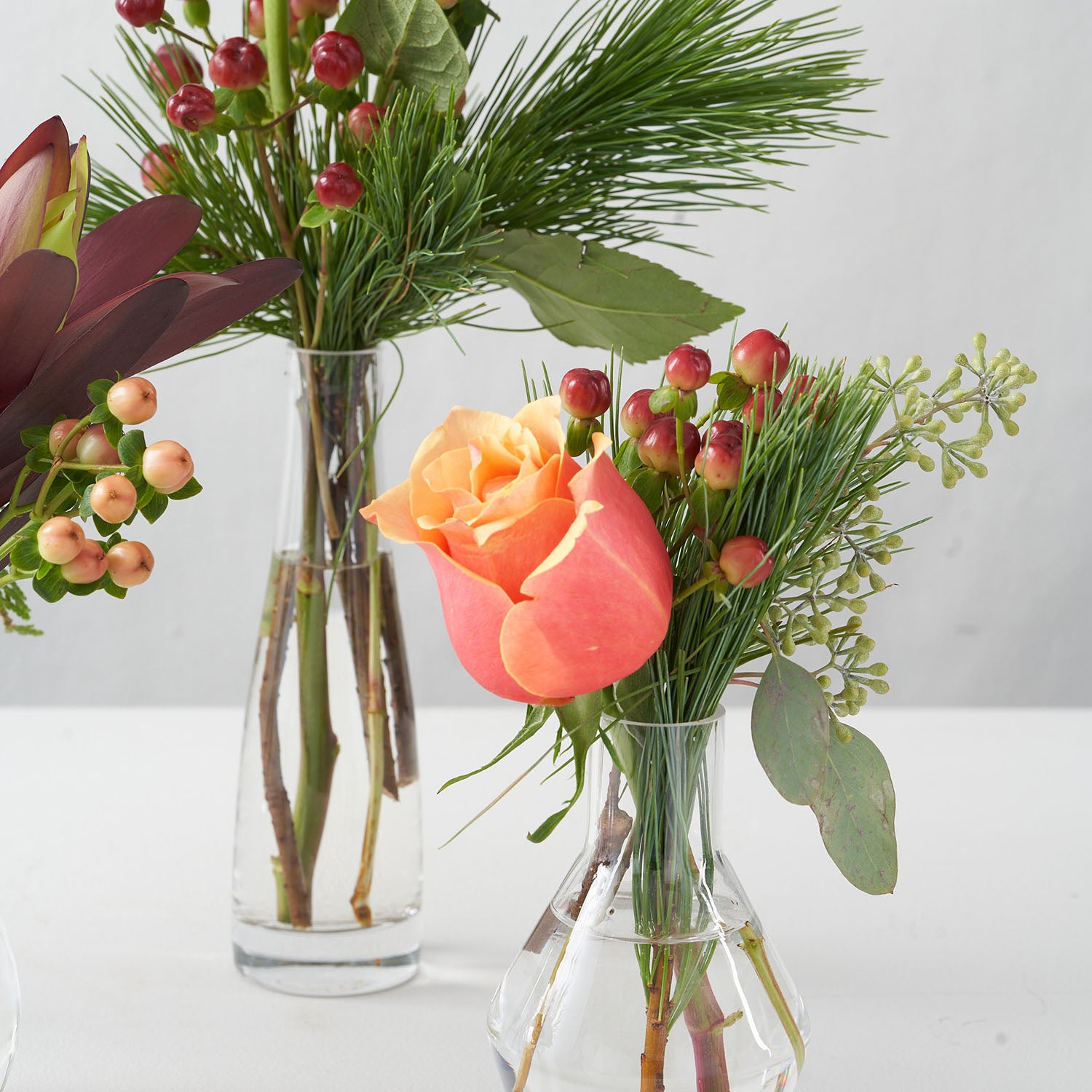 Closeup of small vases with pine, berry eucalyptus, hypericum berries, and Cherrybrandy peach rose.