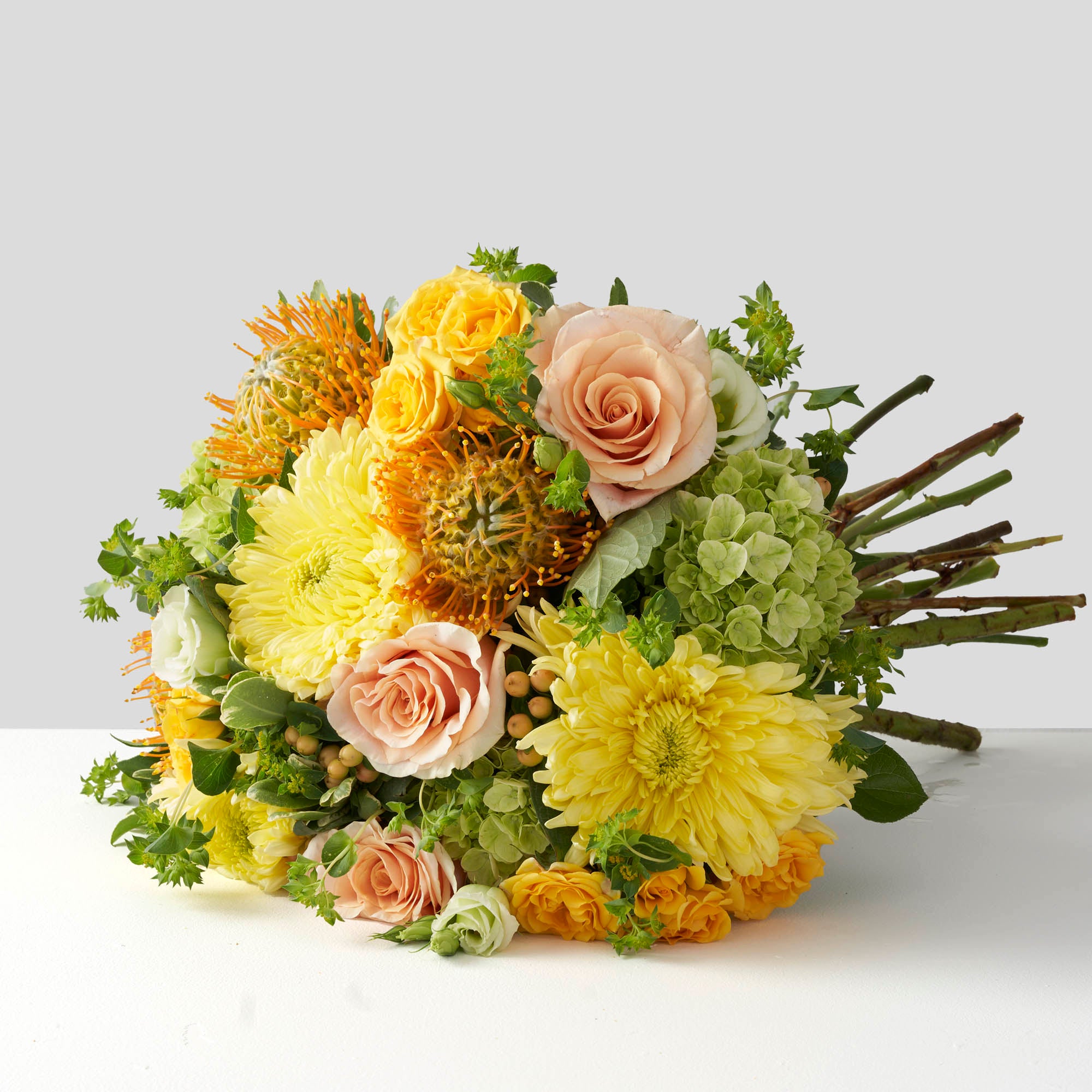 Bouquet of yellow chrysanthemums, peach roses, green hydrangea, peach hypericum berries and gold protea flowers on white background.
